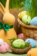 Easter decorative eggs in nest with moss, in basket, on table with yellow bunny and green grass.
