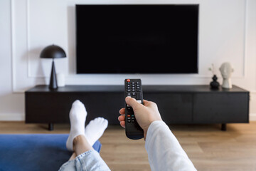 Woman hand hold remote control, turn on tv panel and relaxing on comfort sofa