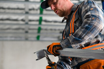 a construction worker in overalls, gloves and a tool belt cuts an iron profile for plasterboard...