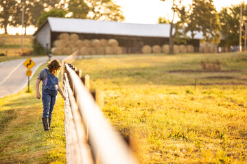 Girl walking fence line of horse pasture in overalls and boots © Npsphoto