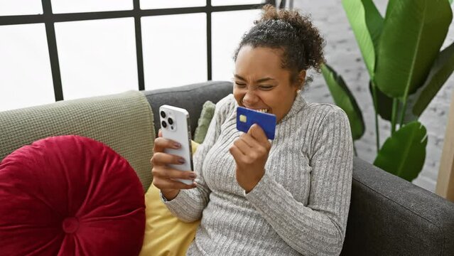 Smiling woman shopping online with credit card and smartphone at home, conveying joy and modern lifestyle.
