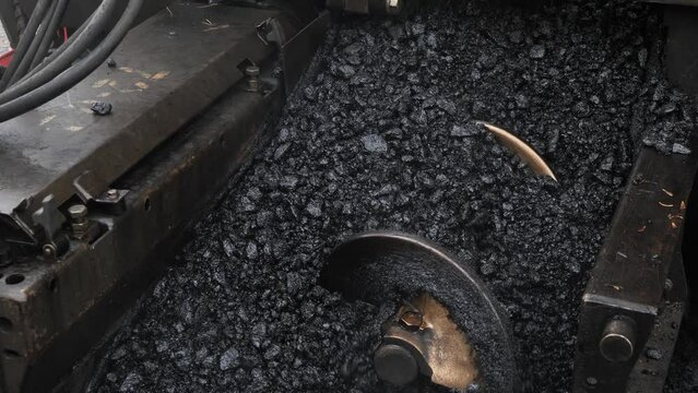 Asphalt paver conveyor unloads hot asphalt, bitumen onto road close-up, paving