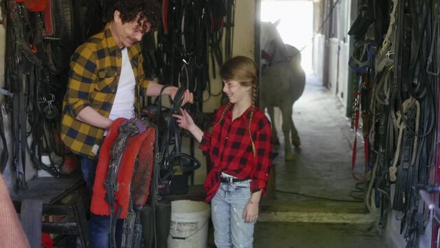Father and daughter are working in the workshop with equipment for horses, preparing the horse for riding