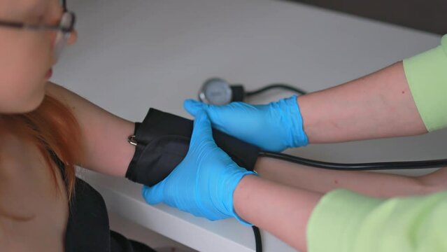 The doctor measures the girl's blood pressure in the clinic.