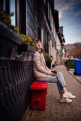 With a thoughtful gaze, a young woman enjoys a peaceful break on a red bench, set against the...