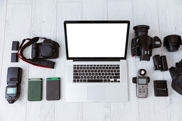 Hipster freelance photography equipment, laptop, smartphone and notebook on a white wooden desktop, flat lay banner with copy space. Laptop with blank screen