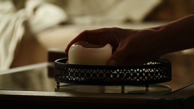 Close-up view of woman's hand arranging three candles on tray on table. Interior design, relaxing environment
