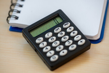 A calculator and a notebook on a wooden table with copy space. Selective focus.