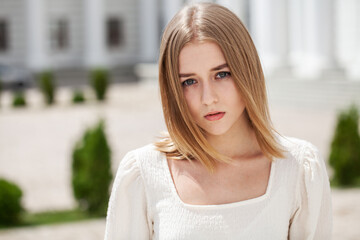 Portrait of a young beautiful blonde girl in a white summer dress with open shoulders