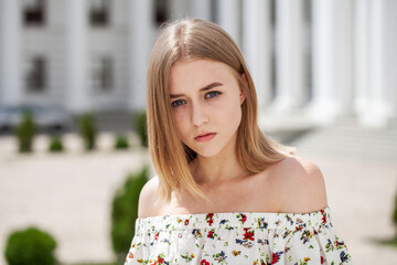 Portrait of a young beautiful blonde girl in a white summer dress with open shoulders