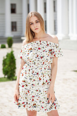 Portrait of a young beautiful blonde girl in a white summer dress with open shoulders