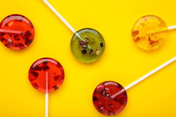 Colorful sweet lollipops with berries on yellow background.