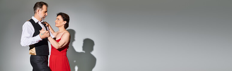 Mature attractive smiling couple dancing ballroom dance isolated on grey background, banner