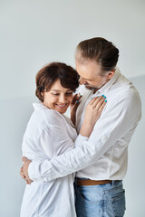 Side view portrait of middle aged couple in love hugging and cuddling on grey backdrop