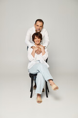 Full length shot of mature beautiful couple sitting on grey background and looking at camera