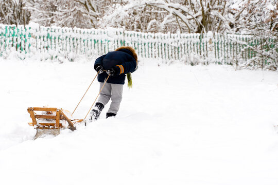 Unrecognizable Boy in forest carries a heap of wood pulling in sleigh 