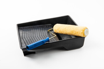 a yellow paint roller with a blue handle and a black plastic paint tray isolated on white