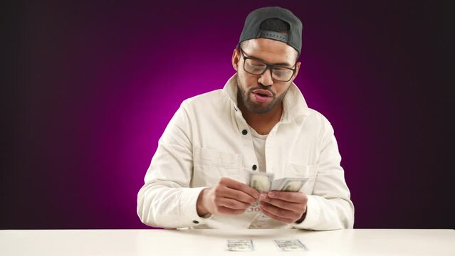 With an infectious grin, a young cryptocurrency millionaire carefully arranges his substantial digital currency profits on a desk, showcasing his successful investments. Camera 8K RAW. 