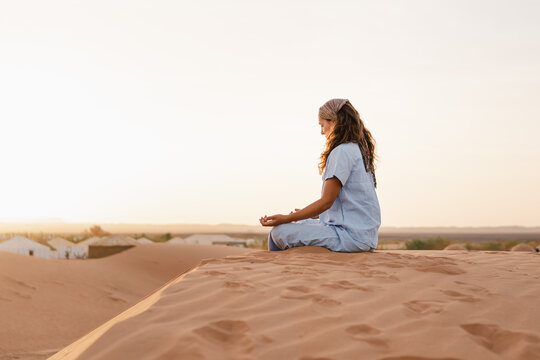 woman sitting on a sand dune, relaxing in a tranquil desert landscape