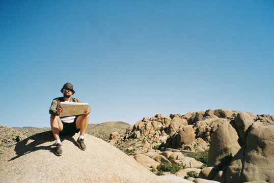 Young man sitting on a rock with a map in a desert 