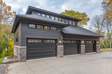 Luxurious new home with a contemporary design, featuring a two-car garage, surrounded by rich charcoal gray siding and a natural stone wall trim for a distinguished appearance. - obrazy, fototapety, plakaty