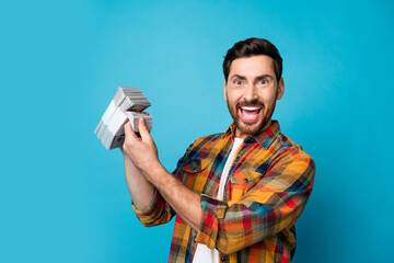 Photo of overjoyed successful man with beard dressed plaid shirt count dollar banknotes scream yeah...