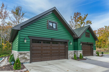 Fototapeta na wymiar Opulent newly constructed home in a contemporary design, featuring a two-car garage, surrounded by striking emerald green siding and a natural stone wall trim.