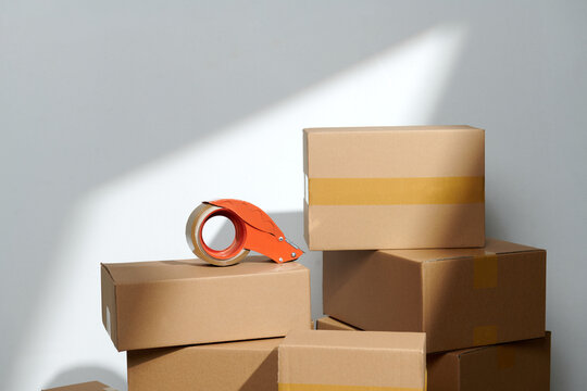 tape dispenser and stack cardboard boxes on floor near white wall