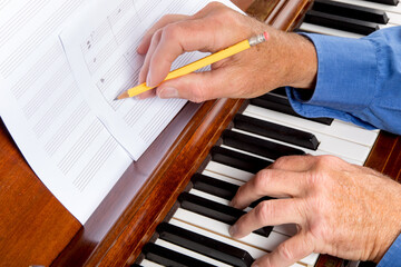 close up of a composer marking notes on staff paper as he plays the piano
