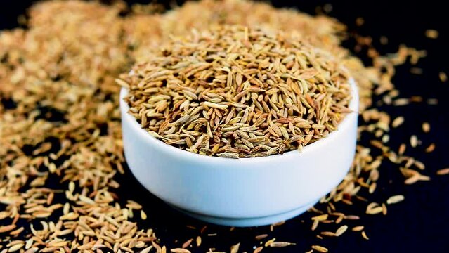 Cumin seeds on a white ceramic bowl on a black background rotation