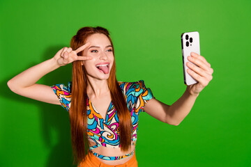 Photo portrait of attractive young woman v-sign tongue out selfie photo dressed stylish retro clothes isolated on green color background