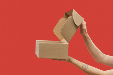 Side view of female hands opening cardboard box over red background