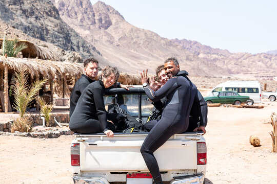 Diverse group of scuba divers sitting at the back of pickup truck