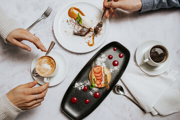 Top down image of two people enjoying coffee and dessert at a table.