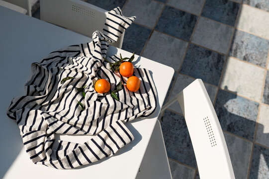 Tangerines and a striped shirt on a white patio table in the sun.