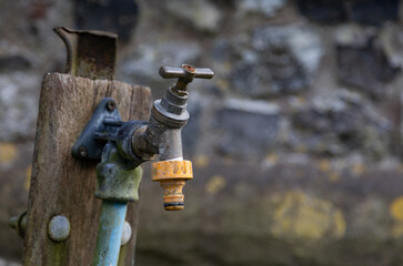 Close-up of a weathered garden tap with a rustic appeal, attached to a mossy wooden post. Can be used as a symbol of water shortage