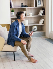 A man enjoys a moment of relaxation with music, seated on a bench in a bright, well-organized living area.