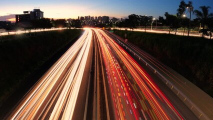 Trail of light caused by vehicular traffic in Highway with buildings from downtown in the background, in Brazil
