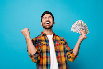 Photo of overjoyed man with beard dressed stylish plaid shirt hold dollars shout clenching fist win...