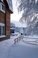 The corner of a brick house, snowdrifts, railings, birch tree branches in the snow. Panorama of a city in the Far North of Russia.