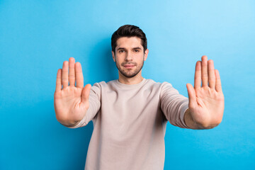 Photo of serious man with stylish haircut dressed beige sweatshirt stretching palms to you showing stop isolated on blue color background