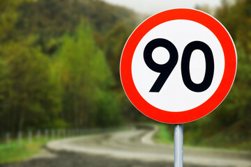 Speed limit sign with curvy road behind. Maximum ninety kilometers per hour. Safety on road...