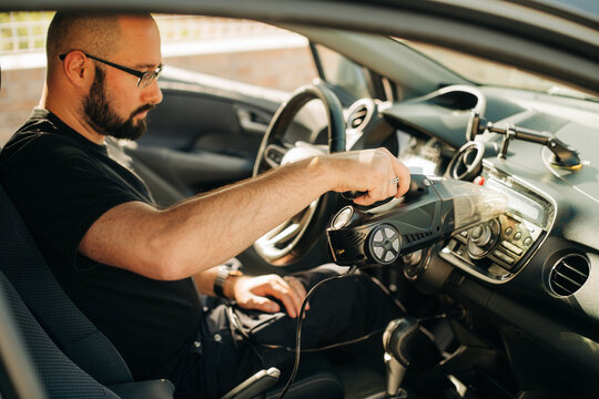 Man cleaning radio in a car with handheld vacuum cleaner