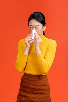 Young woman with tissue sneezing on red background. Runny nose