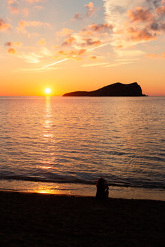 Silhouette of a person sitting on the seashore during a sunset