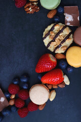 Macarons, chocolate, cookies, berries and various nuts on dark blue background. Top view.