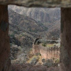 Westerly section of the mighty Kumbhalgarh stone fortress wall (Kumbhalgarh, India) seen from Badal Mahal arrow-slits against a backdrop of eroded barren dry season Aravalli hills