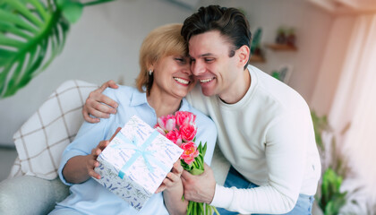 This flowers for my best mom! True bright emotions from mother with her son while sitting on the sofa at living room. Mothers day, birthday or womens day concept - 771004211