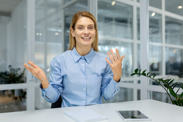 A professional woman in a blue shirt gestures animatedly while looking at a camera, implying a...