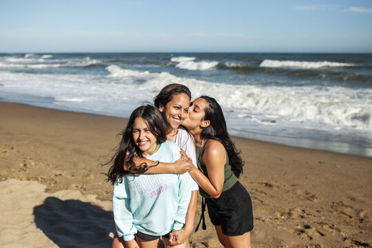 mother cuddling with her two teenage daughters on the beach